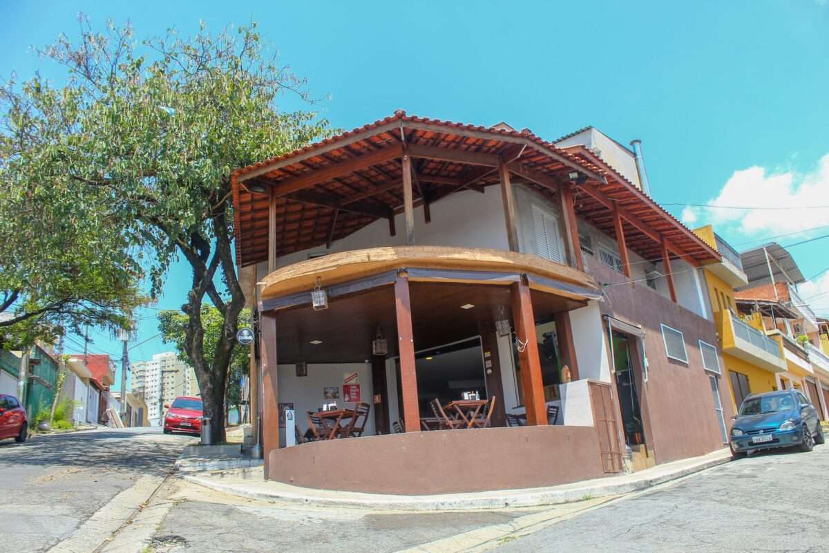 Restaurante de comida nordestina Pezinho no Nordeste. A imagem mostra um sobrado na esquina, de base circular, pintado de marrom e branco, com toldos marrons erguidos.